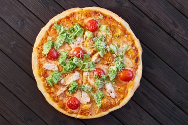 Tavuklu taze pizza, domates ve peynirli koyu ahşap arka planda. Yakın çekim, seçici odaklanma