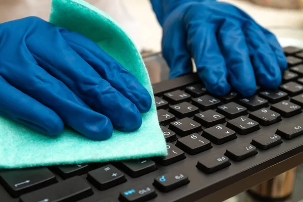 Girl\'s hand in blue protective glove cleans keyboard with a cloth for prevention coronavirus, bacteria, viruses and germs.