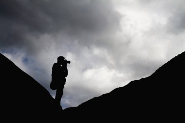 Dağlarda bir adamın silueti manzaranın fotoğraflarını çekiyor.