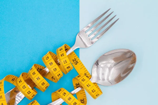 叉子和勺子用带子系在一起 以便在彩色背景上测量 饮食和体重减轻的象征 — 图库照片