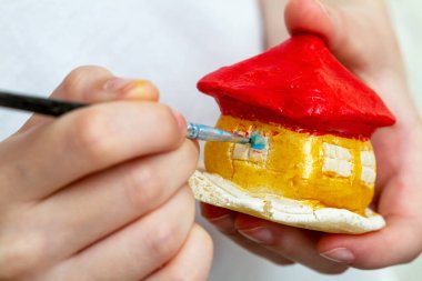 Küçük kız evi kil ya da tuzlu hamurdan akrilik boyalarla boyuyor. Eğitim kavramı.