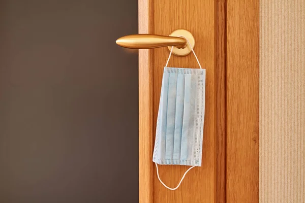 Mavi hijyenik tıbbi yüz koruma maskesi kapı kolunda asılı. Koronavirüs covid-19 salgını sırasında korunma ve güvenlik kavramı. Yakın çekim.