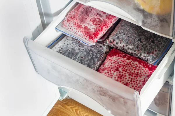 Dondurucuda şeffaf plastik torbalarda donmuş meyveler. Donmuş kırmızı ve siyah akıntılarla dolu derin dondurucuyu aç.