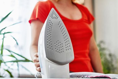 Ütü masasında giysileri ütüleyen bir kadın.