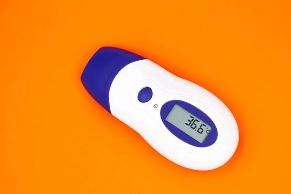 A non-contact infrared thermometer on a orange background showing temperature 36.6