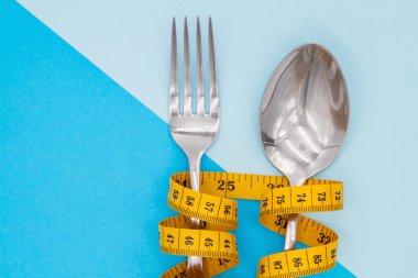Çatal ve kaşık renkli arka planda ölçmek için bir kurdele ile asılır. Diyet ve kilo kaybı sembolü