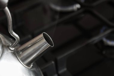 Çelik çaydanlığın bir parçası. Siyah gaz sobasında kaynar su ve yakıcı gaz ocakları var.