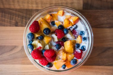 Yoğurtlu renkli meyve salatası, ahşap masada doğal fotoğrafçılık, sağlıklı kahvaltı veya atıştırmalık konsepti.