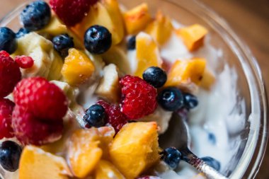Böğürtlenli renkli meyve salatası, ahududu, şeftali ve yoğurt ahşap yüzeyde cam bir kasede, sağlıklı kahvaltı kavramı.