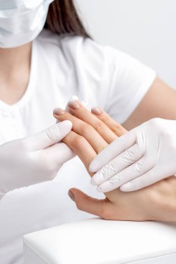 Manikürcü kadının elini tutuyor, tırnaklarına bej oje sürmüş, kapat..