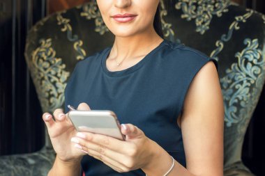 İş kadını akıllı telefon kullanıyor. Evden çalışıyor. Koltukta oturuyor ve kameraya bakıyor..