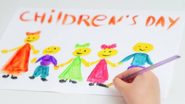 Çocuk eli beyaz bir kağıtta farklı renkte çocukları kelimelerle çiziyor..