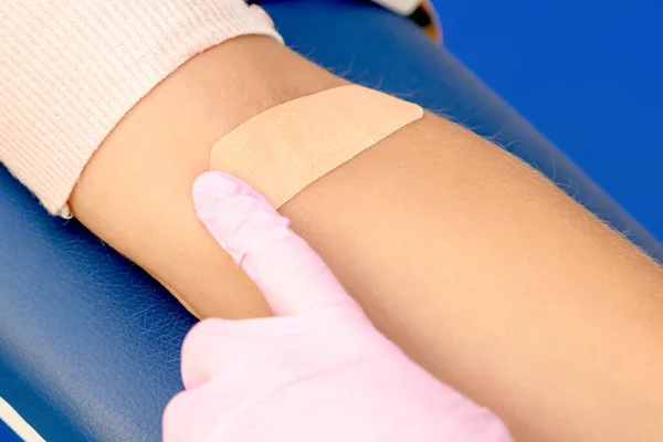 Nurse hand is glueing an adhesive plaster on arm, close up.