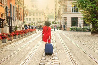 Güzel genç kız eski Avrupa şehrinin tramvay yolunda mavi bavuluyla yürüyor..