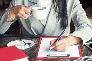 Deftere yazı yazan ve kafede kahve içen tanınmamış bir kadının elleri. Kafede öğle yemeği molasında olan iş kadını..