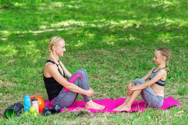 stock image Mother and her daughter sitting on a roll mat in the public park.