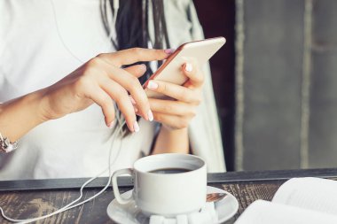 Kafede cep telefonunu kullanan genç bir kadının elleri..