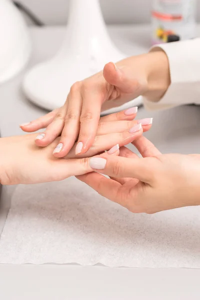 Hands and nails of young woman receiving oil massage by beautician at beauty salon.