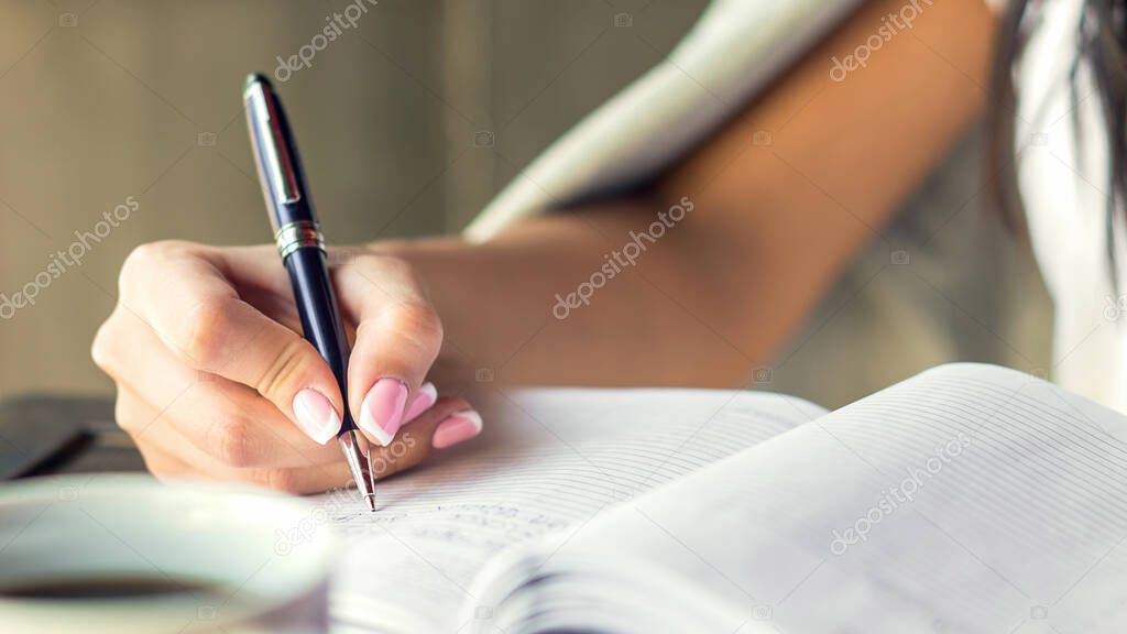 Young woman right hand writing plans on small diary in cafe close up. Business concept