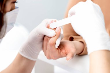 Manikürcüde manikür yaptıran genç bir kadın. Manikürcü müşterinin tırnaklarını törpülüyor