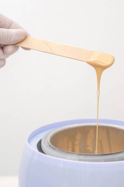 Balmumu ısıtıcısı ve insan eliyle ahşap spatula. Tüy dökümü için sıcak mum. Salon ekipmanları