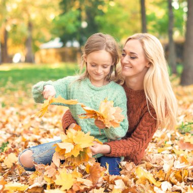 # Mutlu, genç, beyaz anne ve küçük kızı # # Sonbahar sarısı yapraklarıyla parkta oturuyorlar #