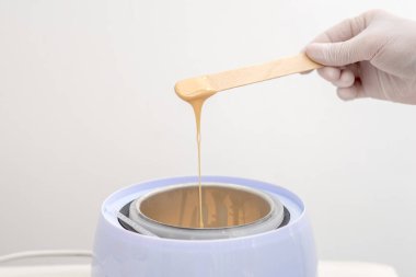 Balmumu ısıtıcısı ve insan eliyle ahşap spatula. Tüy dökümü için sıcak mum. Salon ekipmanları