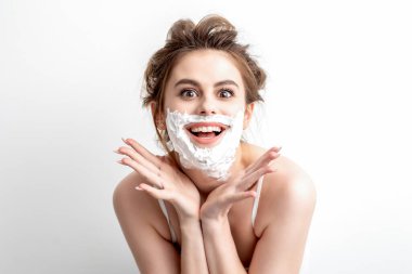 Yüzünde tıraş köpüğü olan beyaz arka planda poz veren güzel beyaz bir kadın.