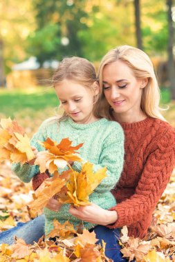 # Mutlu beyaz kadın ve küçük kız # # Sonbahar sarısı yapraklarıyla parkta oturuyorlar #