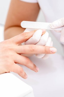 Manikürcüde manikür yaptıran genç bir kadın. Manikürcü müşterinin tırnaklarını törpülüyor