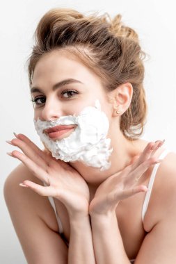 Yüzünde tıraş köpüğü olan beyaz arka planda poz veren güzel beyaz bir kadın.