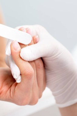 Manikürcüde manikür yaptıran genç bir kadın. Manikürcü müşterinin tırnaklarını törpülüyor