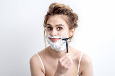 Beyaz arka planda jiletle yüzünü tıraş eden güzel beyaz bir kadın. Yüzünde tıraş köpüğü olan güzel bir kadın.