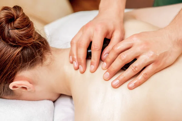 Hands of massage therapist doing back massage with massage stones on back of woman close up.