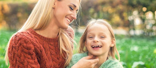 美丽的年轻的高加索母亲和小女儿在秋天公园的绿草上微笑着 — 图库照片