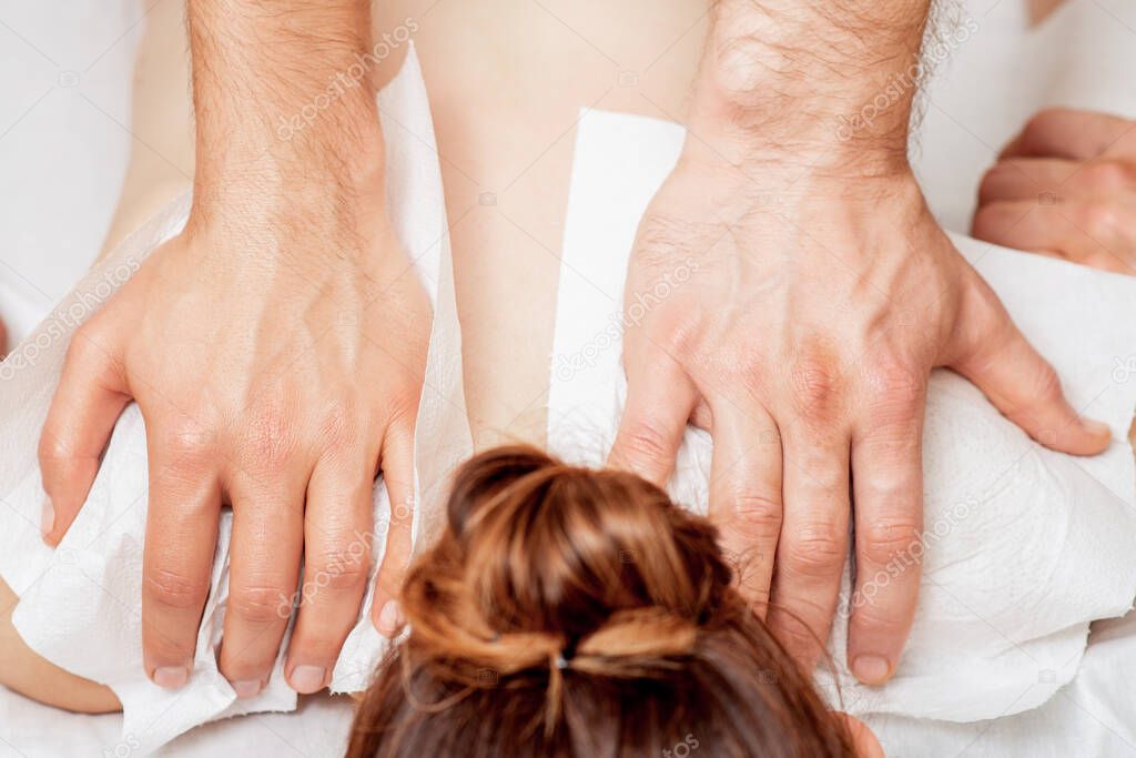 Back massage on back of woman in four hands by two male therapists.
