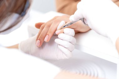 Manikürcünün manikür salonundaki kadın tırnaklarını sökmek için manikür makası kullanmasını kapat.