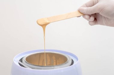 Balmumu ısıtıcısı ve insan eliyle ahşap spatula. Tüy dökümü için sıcak mum. Salon ekipmanları