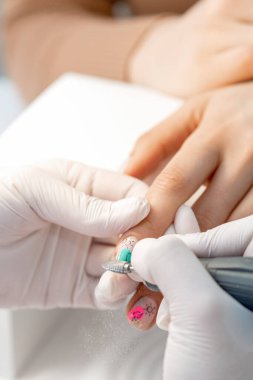 Manikür ustası, manikür salonundaki ojeli elleri çıkarmak için elektrikli tırnak makinesi kullanıyor.