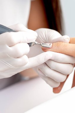 Manikür ustası, manikür salonundaki ojeli elleri çıkarmak için elektrikli tırnak makinesi kullanıyor.