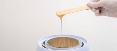 Balmumu ısıtıcısı ve insan eliyle ahşap spatula. Tüy dökümü için sıcak mum. Salon ekipmanları