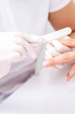 Manikürcüde manikür yaptıran genç bir kadın. Manikürcü müşterinin tırnaklarını törpülüyor