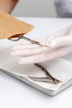 Manikürcü elleri, beyaz masanın manikür prosedüründen önce el işi zarfından manikür aletlerini alıyor.