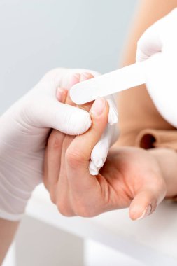 Manikürcüde manikür yaptıran genç bir kadın. Manikürcü müşterinin tırnaklarını törpülüyor