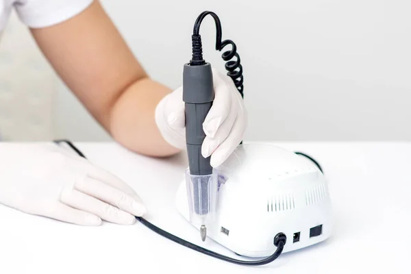 Electric manicure machine in manicure master hand at the white table. Drill for manicure