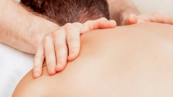 Young man receiving back massage by hands of masseur in spa beauty salon.