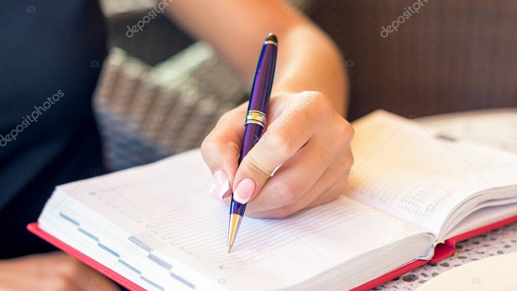 Woman hand is writing business plan on small notebook at outdoor area at cafe. Business concept.