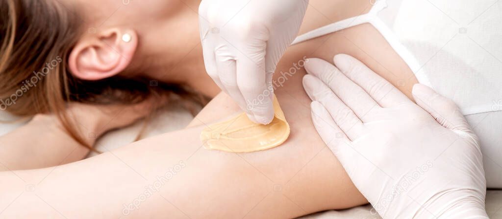 Hand of cosmetologist applying wax paste on armpit. Depilation or epilation female armpit with liquid sugar paste. Smooth underarm concept