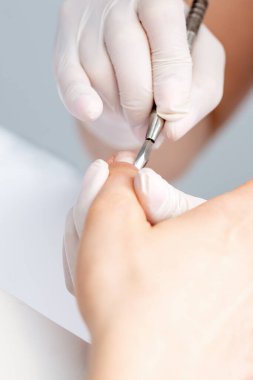 Manikürcünün elleri manikür aletini dişinin tırnaklarına bastırıyor. Manikür ve manikür yaptıran bir kadın.