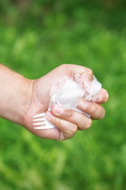 Parktaki yeşil çimlerin arka planında plastik kap kacak tutan bir adamın eli.